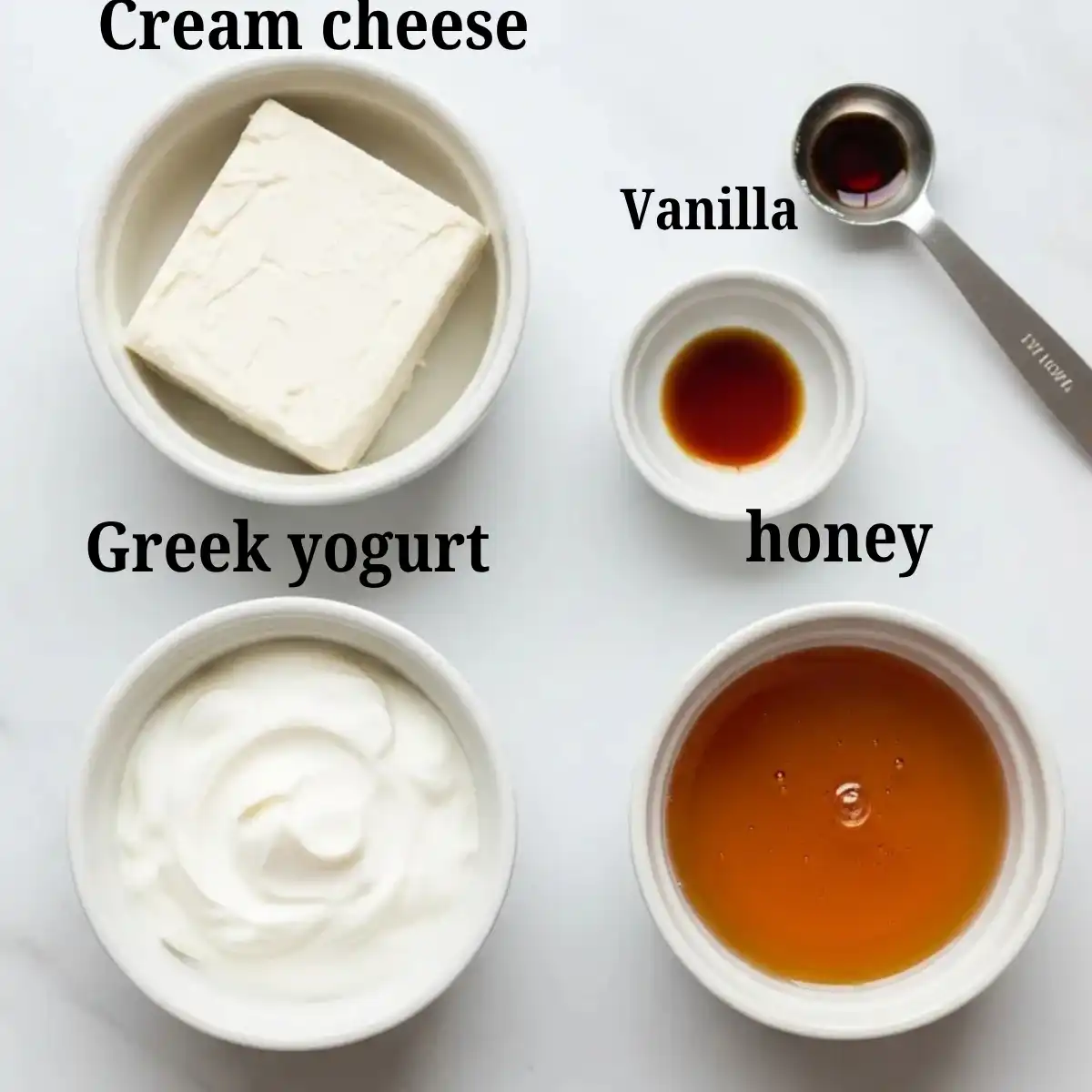 Flat lay of ingredients for a light cream cheese frosting, including cream cheese, Greek yogurt, maple syrup, and vanilla extract in small white bowls on a marble background.