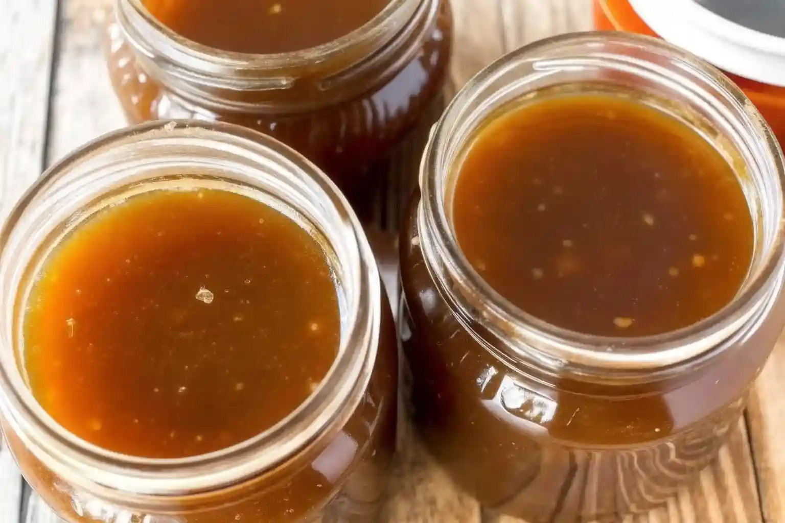 Golden homemade beef broth stored in glass Mason jars on a rustic wooden table, ready for soups, stews, or meal prep.