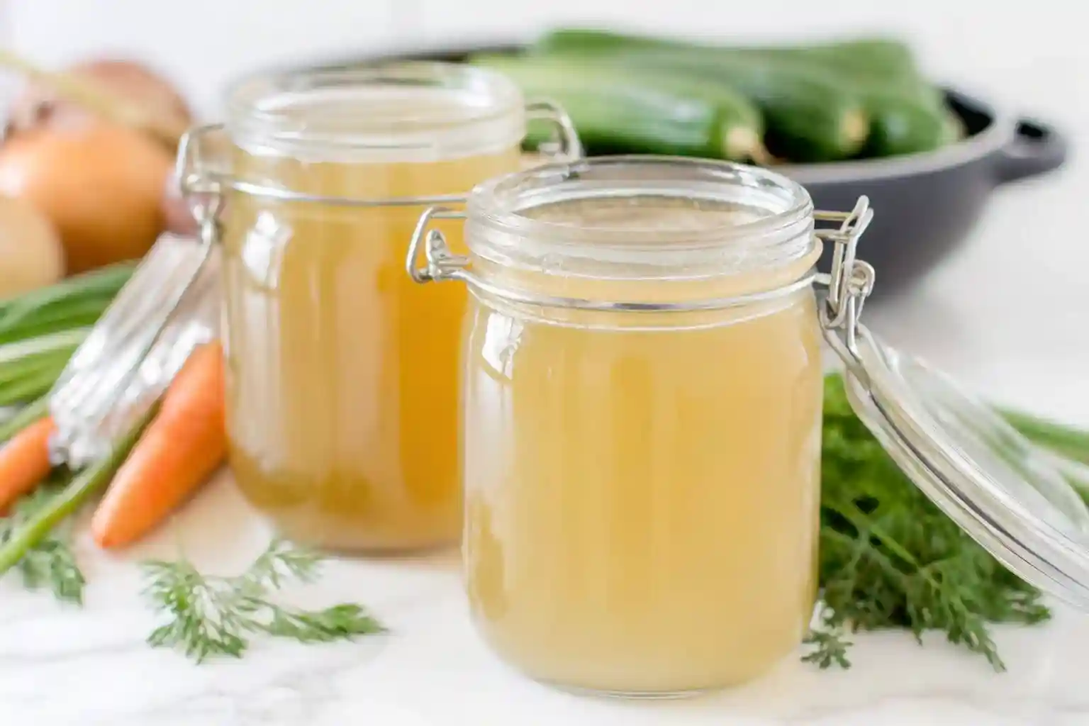 A bright, clean overhead flat lay of A clear glass bowl filled with smooth light golden yellow homemade broth, no herbs or garnish, clean glossy surface with tiny natural bubbles, warm natural lighting, placed on a rustic wooden table, cozy modern kitchen background softly blurred, professional high-detail food photography, crisp focus, bright and inviting atmosphere.