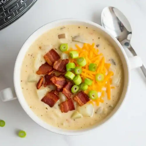 Bowl of creamy crockpot potato soup topped with turkey bacon, cheese, and green onions.
