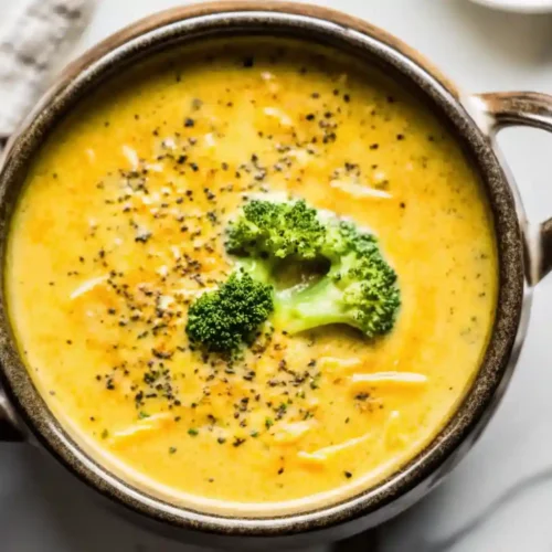 Creamy broccoli cheese soup in a rustic bowl topped with fresh broccoli florets and cracked black pepper.