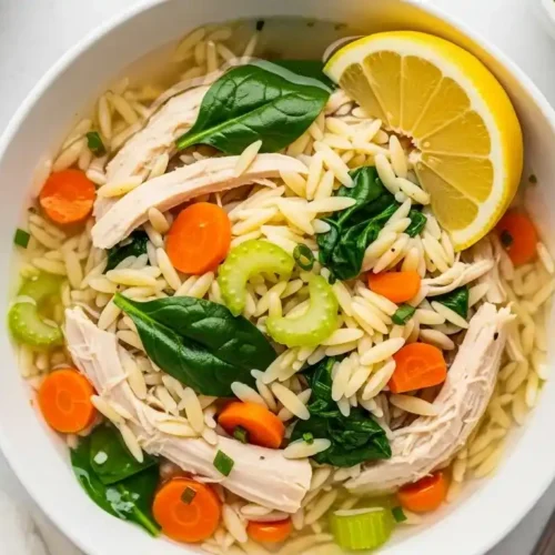 Bright bowl of crockpot lemon chicken orzo soup with chicken, orzo, lemon, and spinach.