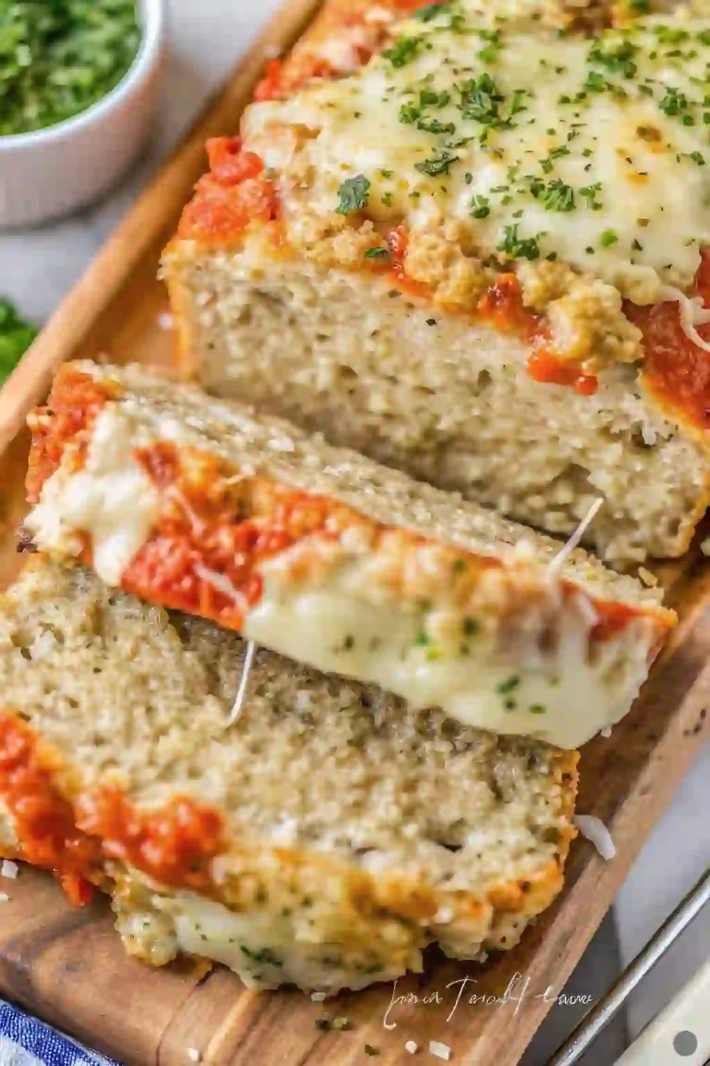 A close-up view of parmesan chicken meatloaf served in thick slices, layered with marinara sauce and melted mozzarella cheese, then finished with a lightly golden topping for a comforting Italian-inspired dinner.
