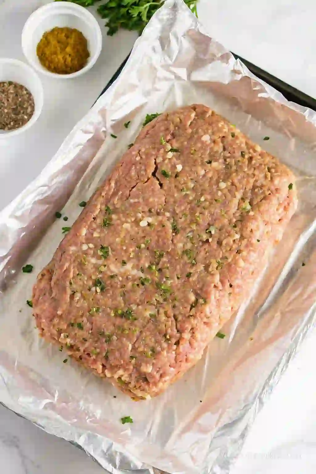 Raw chicken meatloaf shaped into a loaf on a lined baking pan