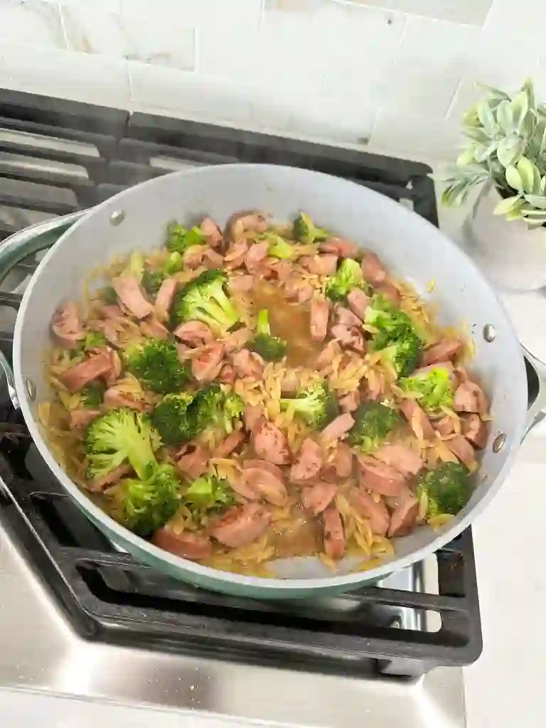 add-broccoli-garlic-orzo-broth._compressed Chicken sausage, broccoli, and orzo simmering together in a skillet