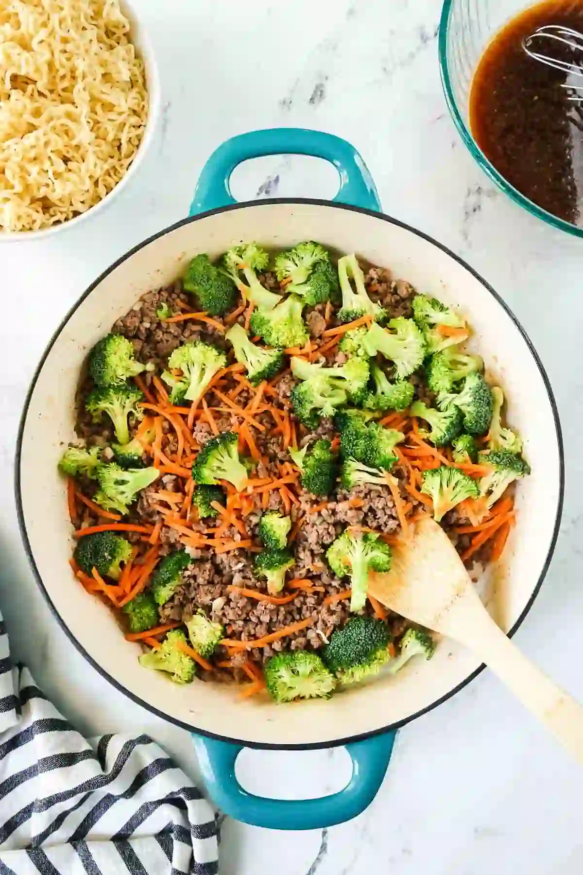 Broccoli and shredded carrots cooking with ground beef in a skillet