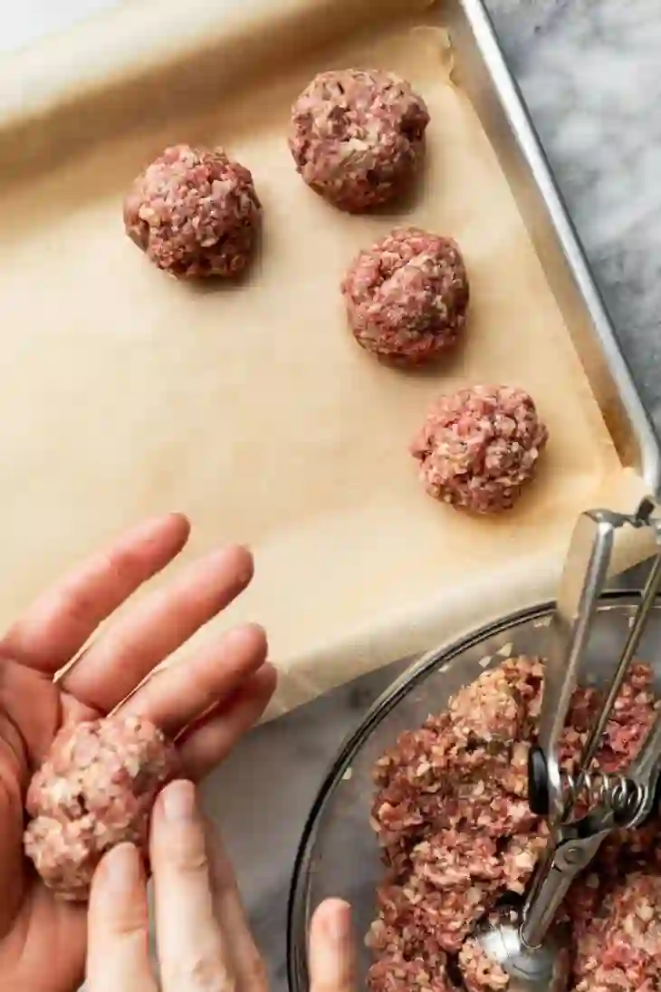 baked-italian-meatballs-step-2-form-meatballs._compressed Forming raw Italian meatballs into evenly sized balls on a parchment-lined baking sheet