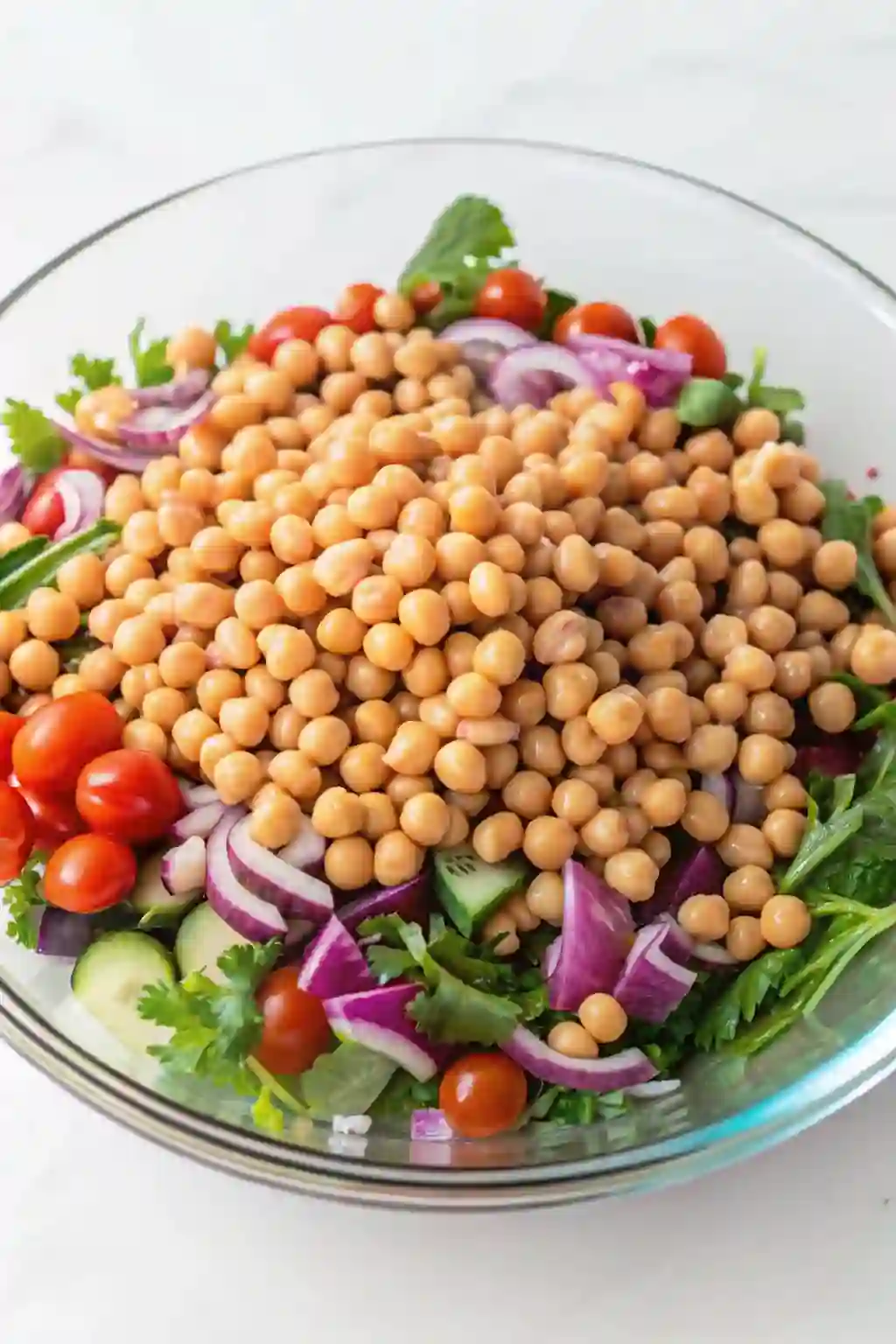 Rinsed chickpeas tossed with cucumber, tomatoes, red onion, and arugula in a large bowl.