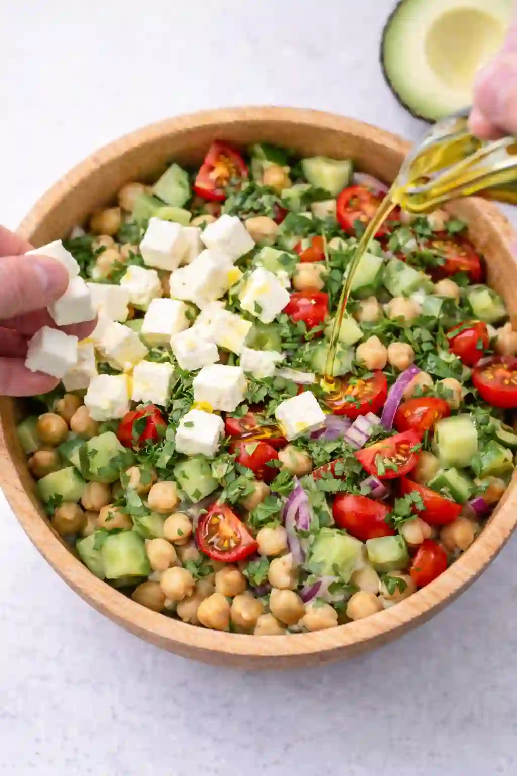 Adding cubed feta cheese and olive oil to chickpea avocado salad