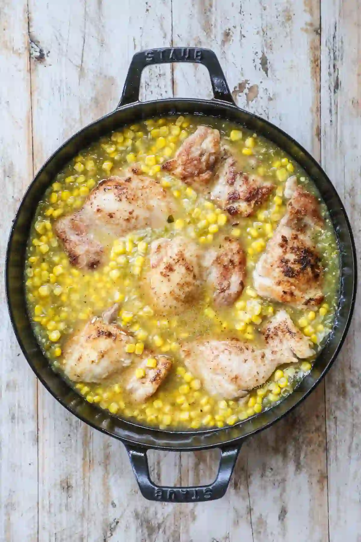 Chicken thighs simmering with rice and corn in a skillet.