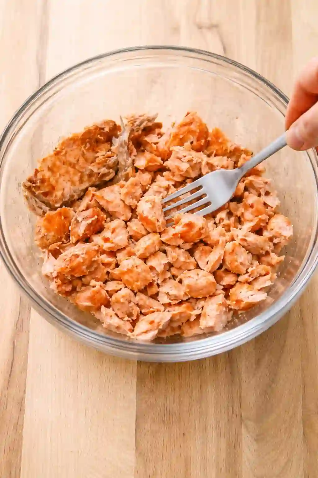 Flaking cooked salmon into small pieces in a glass bowl
