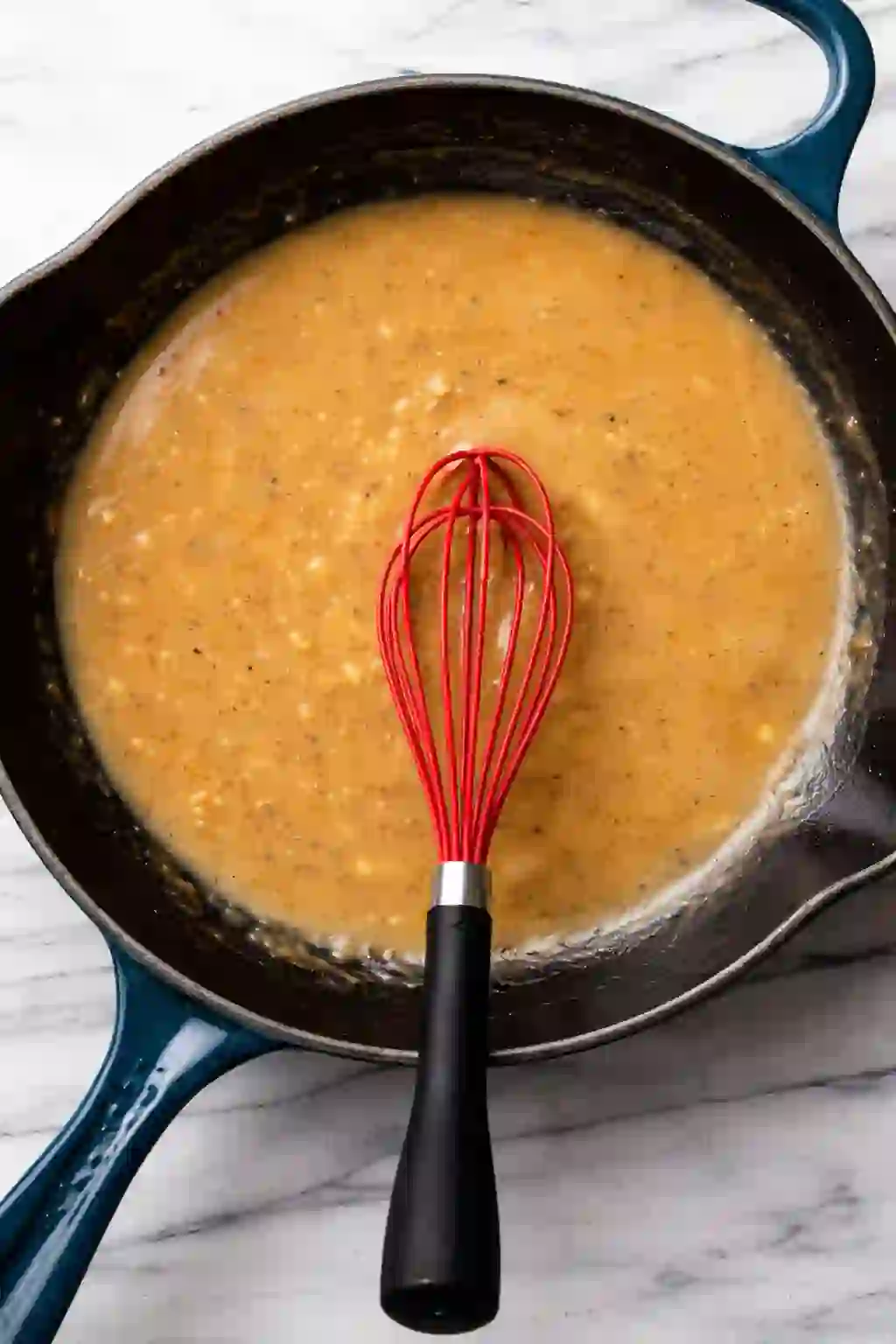 Creamy garlic Parmesan sauce being whisked in a cast iron skillet.