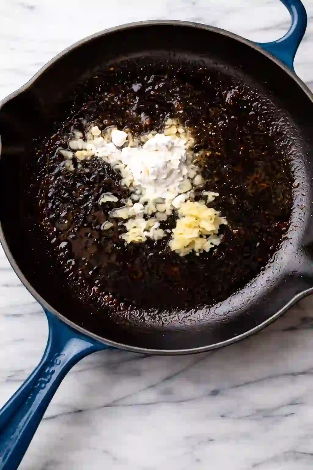 Flour and minced garlic added to a hot skillet with browned bits to start a creamy sauce.