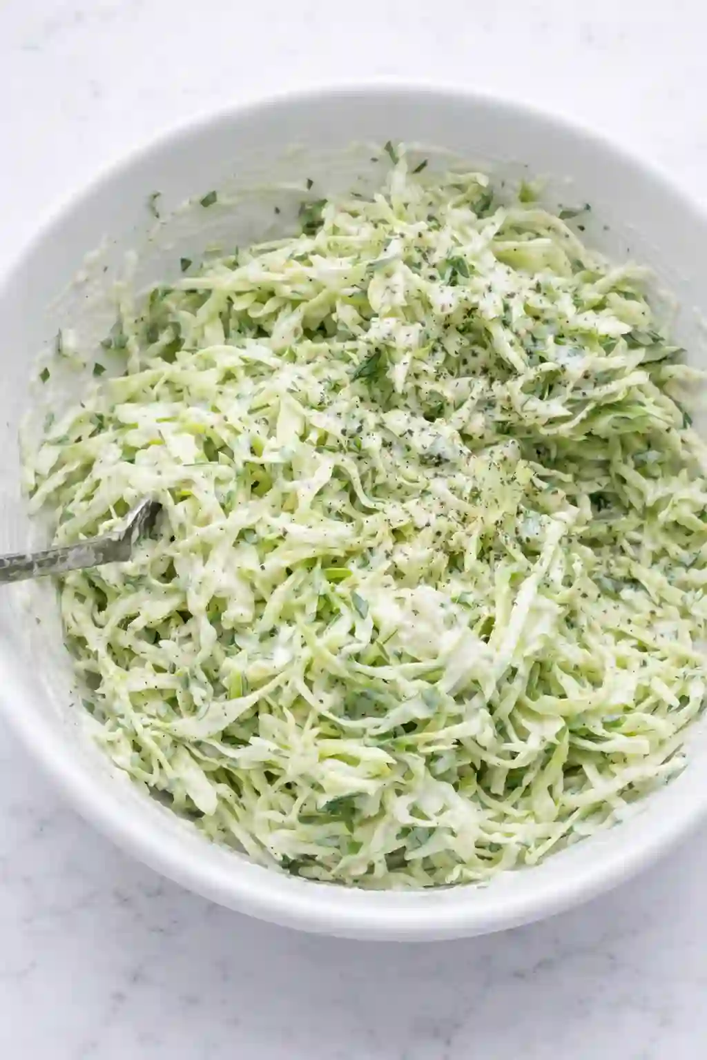 Creamy herby ranch slaw with shredded cabbage and fresh herbs in a white bowl on a white table background