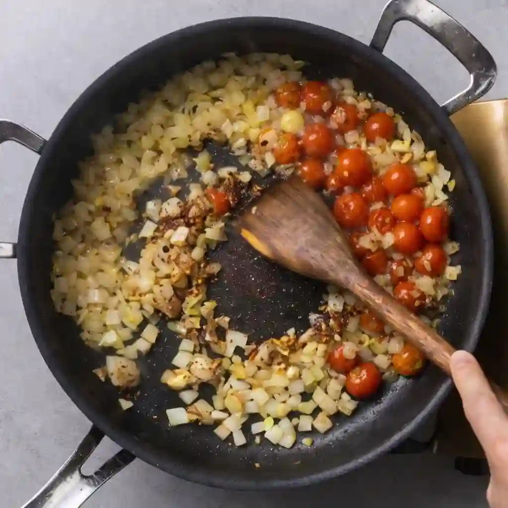 mediterranean-chicken-orzo-step-2-saute-aromatics._compressed (1) Onions, garlic, and cherry tomatoes sautéing in olive oil in a skillet