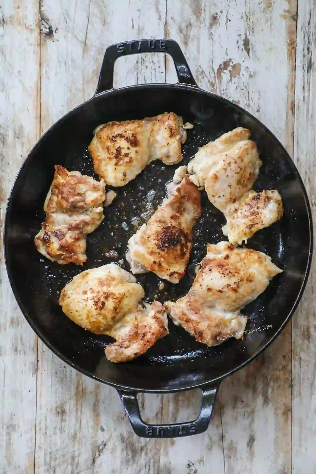 Sear-browned chicken thighs cooking in a cast iron skillet.