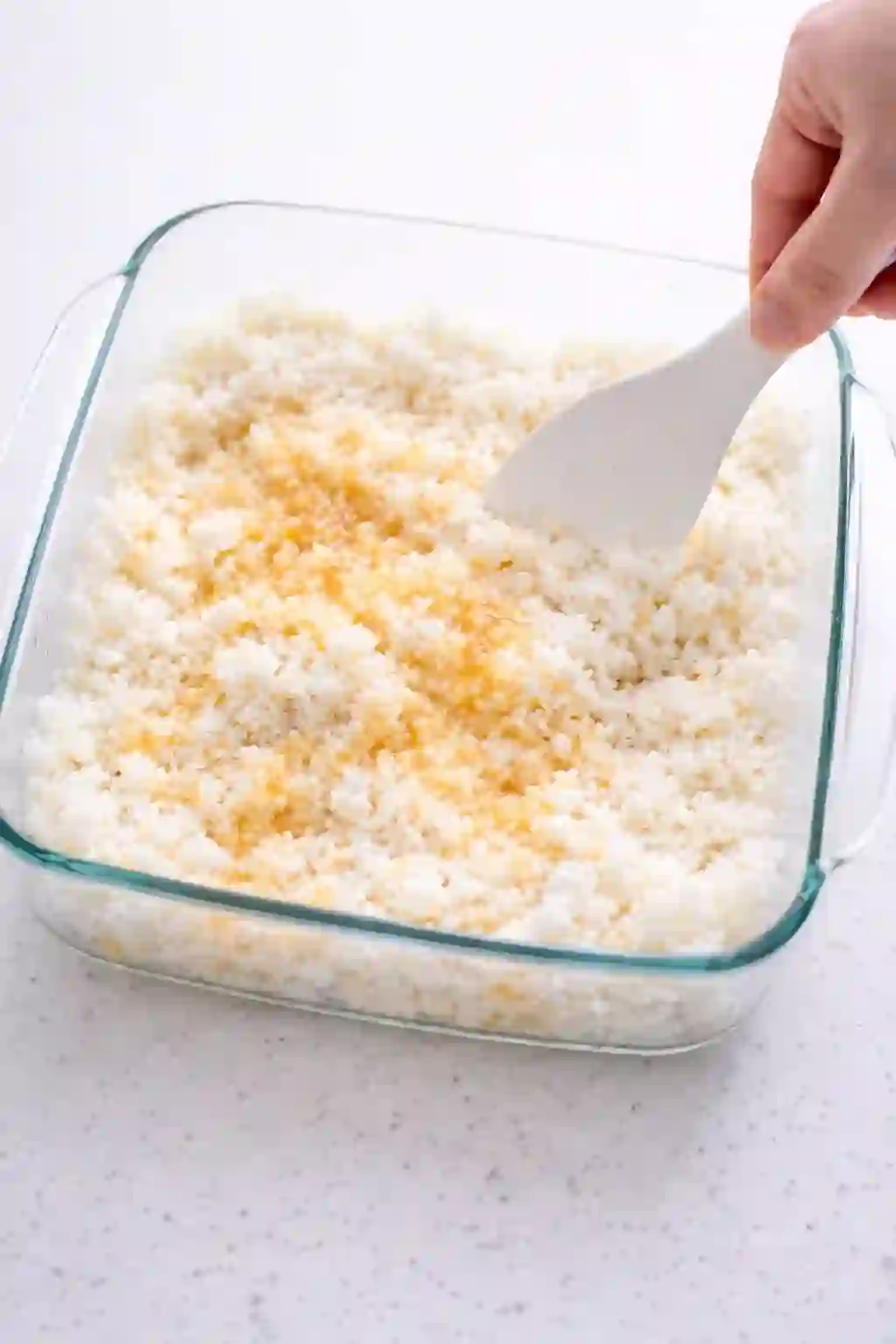 Seasoning sushi rice with vinegar mixture using a rice paddle in a baking dish
