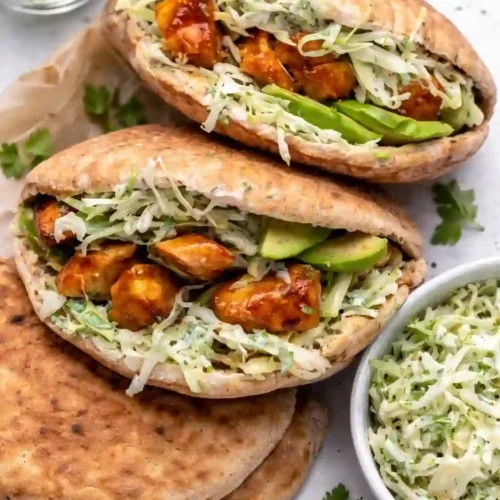 Sheet pan chicken pitas filled with caramelized chicken, herby ranch slaw, and avocado on a white table background