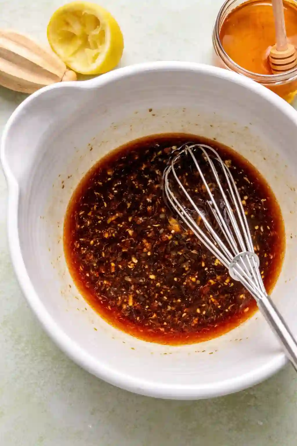 sheet-pan-honey-garlic-shrimp-step-1make-sauce.webp_compressed Honey garlic sauce being whisked in a white bowl with lemon and honey nearby