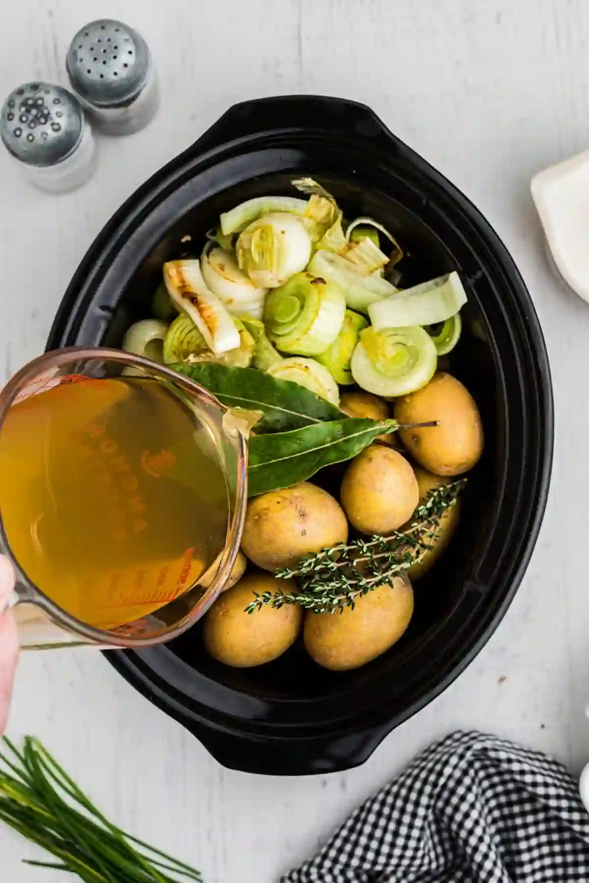 slow-cooker-potato-leek-soup-step-2._compressed Adding chicken broth to a slow cooker with potatoes, leeks, and herbs
