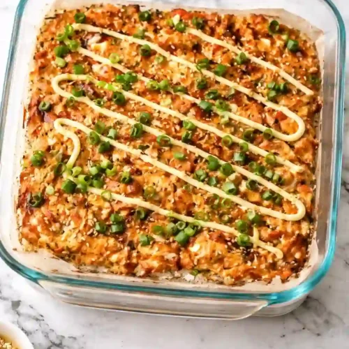 Spicy salmon sushi bake topped with green onions and spicy mayo in a glass baking dish