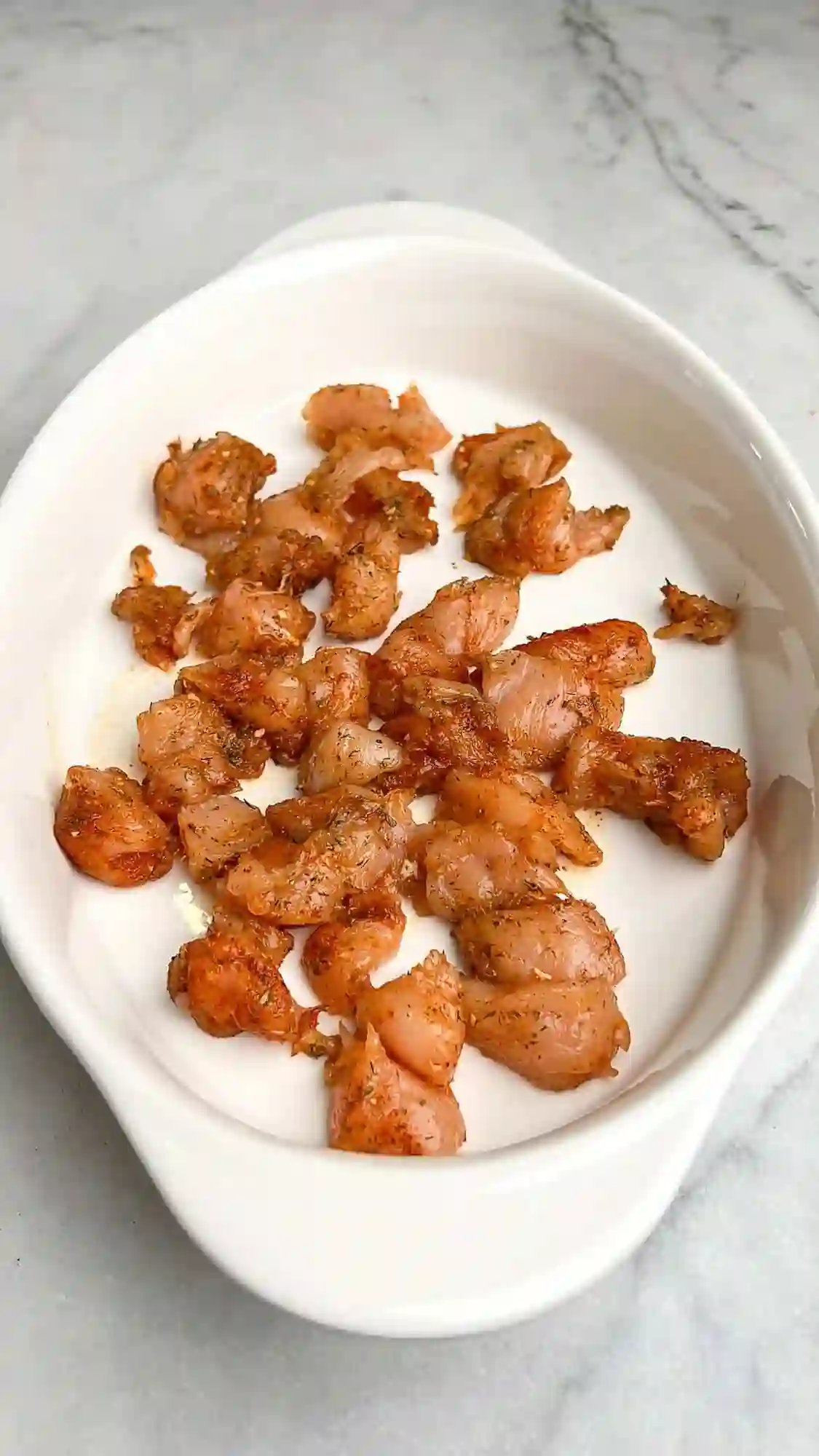 step-2-season-chicken-casserole._compressed Seasoning diced chicken breast with spices in a casserole dish before baking.