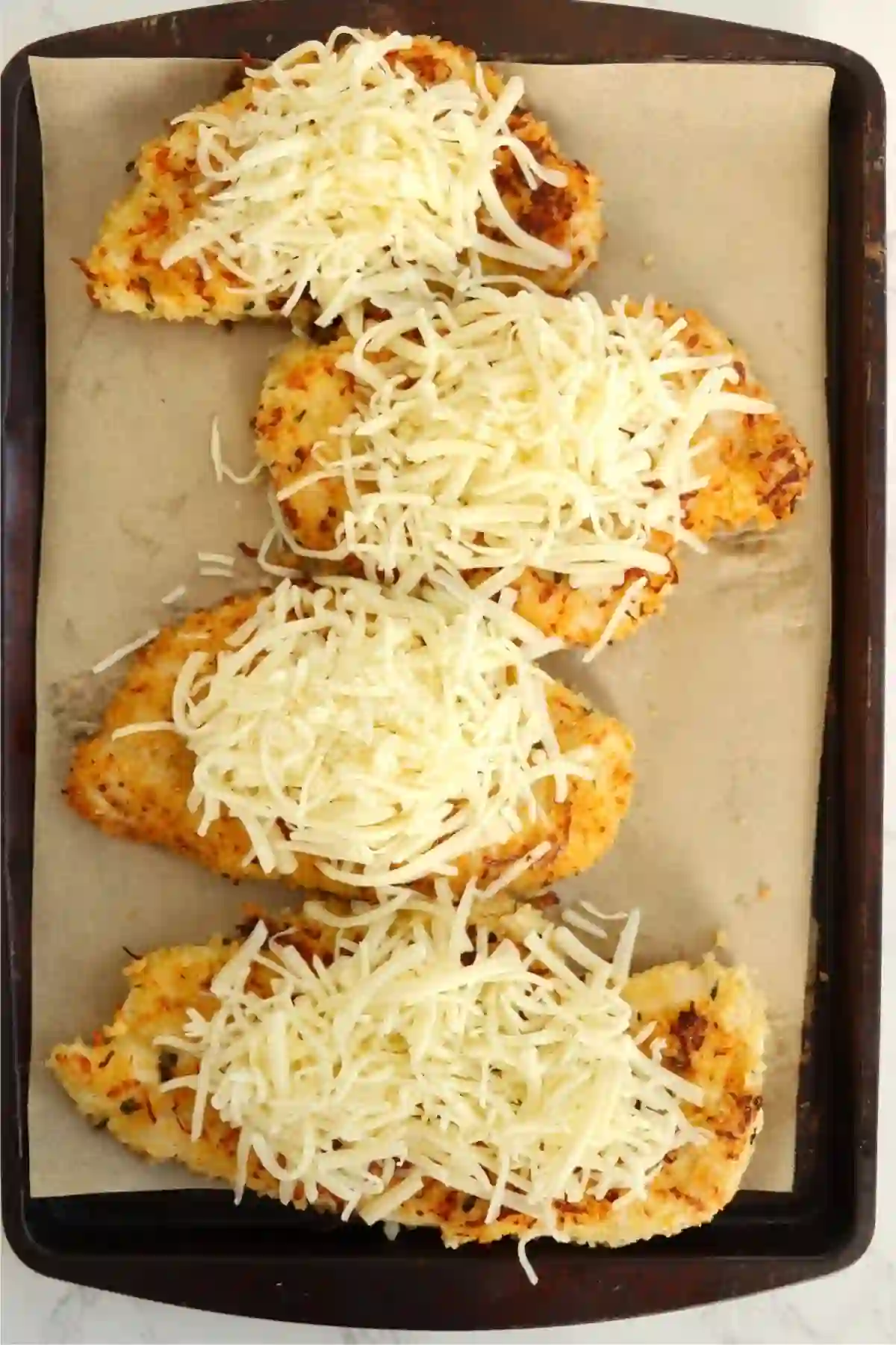 step-4-add-cheese-bake._compressed Chicken topped with melted cheese on baking sheet