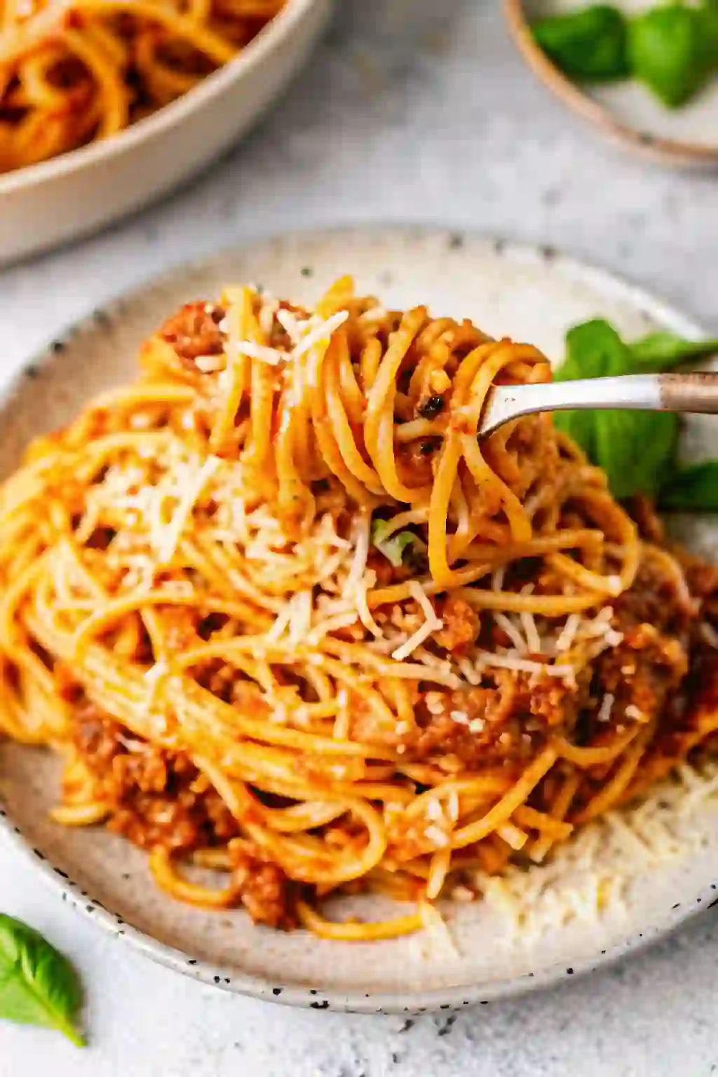 Fork twirling spaghetti bolognese with rich meat sauce and grated cheese on a plate.