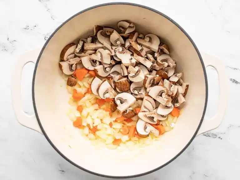 add-mushrooms-to-pot_compressed Sliced mushrooms added to sautéing vegetables in a large pot.