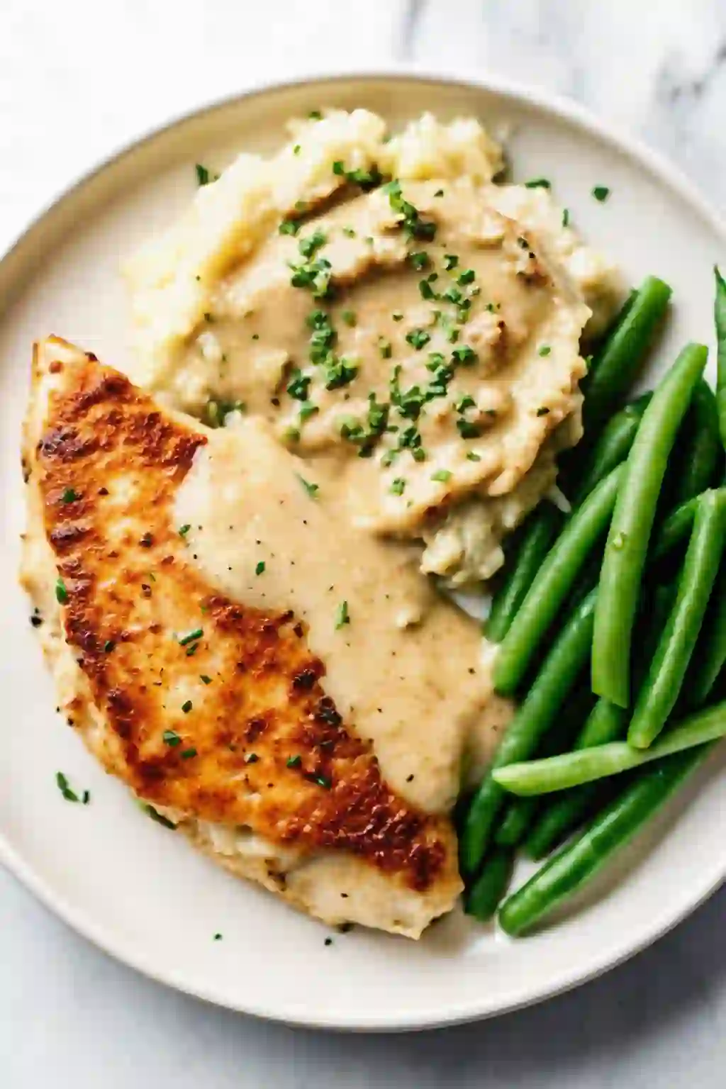 Garlic Parmesan chicken served with mashed potatoes and green beans on a white plate.