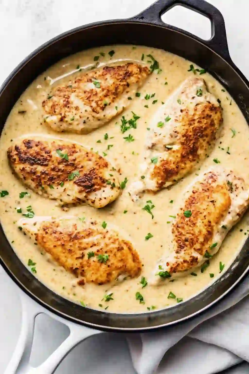 Garlic Parmesan chicken cooking in a creamy sauce in a cast iron skillet.