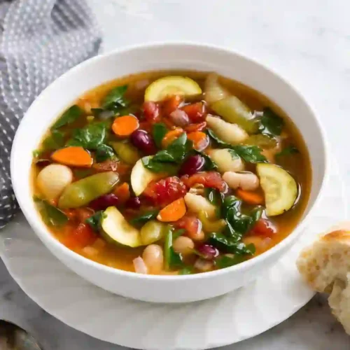 Crockpot minestrone soup with vegetables, beans, and pasta served in a white bowl.