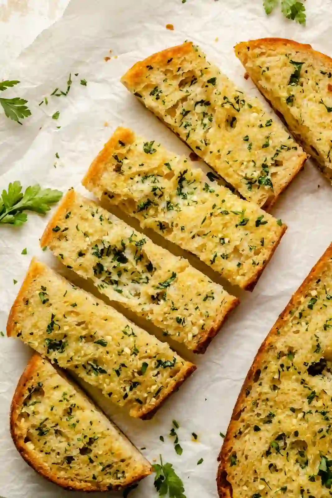 Sliced crusty garlic bread with golden edges and buttery garlic topping on parchment paper