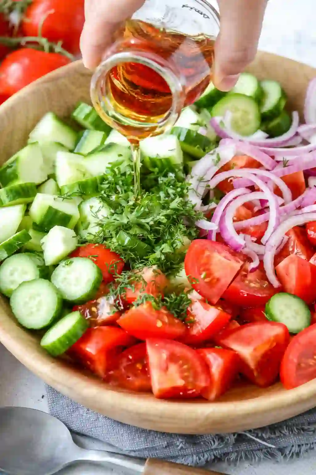 cucumber-tomato-salad-mixing._compressed Pouring red wine vinegar over cucumber, tomato, and red onion salad ingredients in a wooden bowl