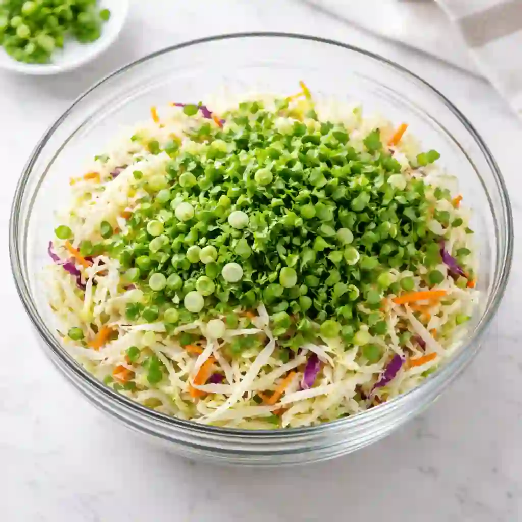 easy-cilantro-lime-slaw-step-1._compressed (1) Coleslaw mix with green onions and cilantro in a mixing bowl on white table
