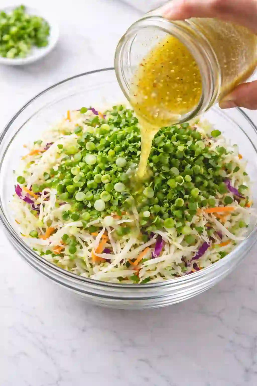 easy-cilantro-lime-slaw-step-3._compressed (1) Cabbage slaw being tossed with lime dressing in glass bowl on white table
