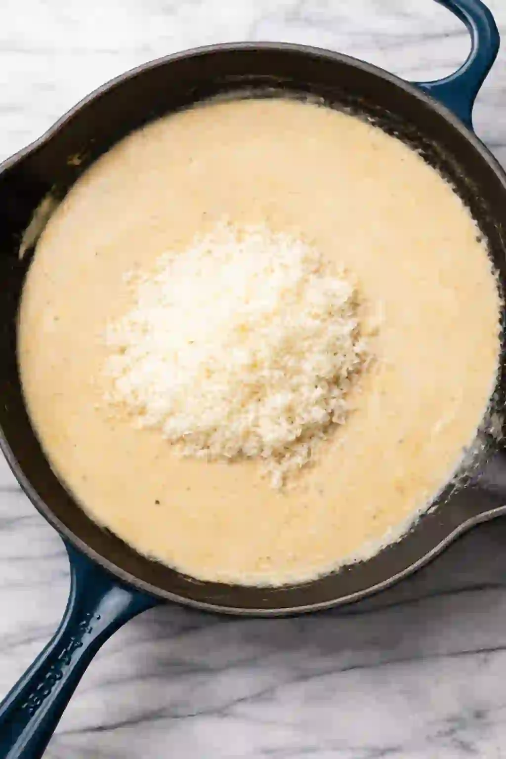 Freshly grated Parmesan cheese added to a creamy garlic sauce in a cast iron skillet.
