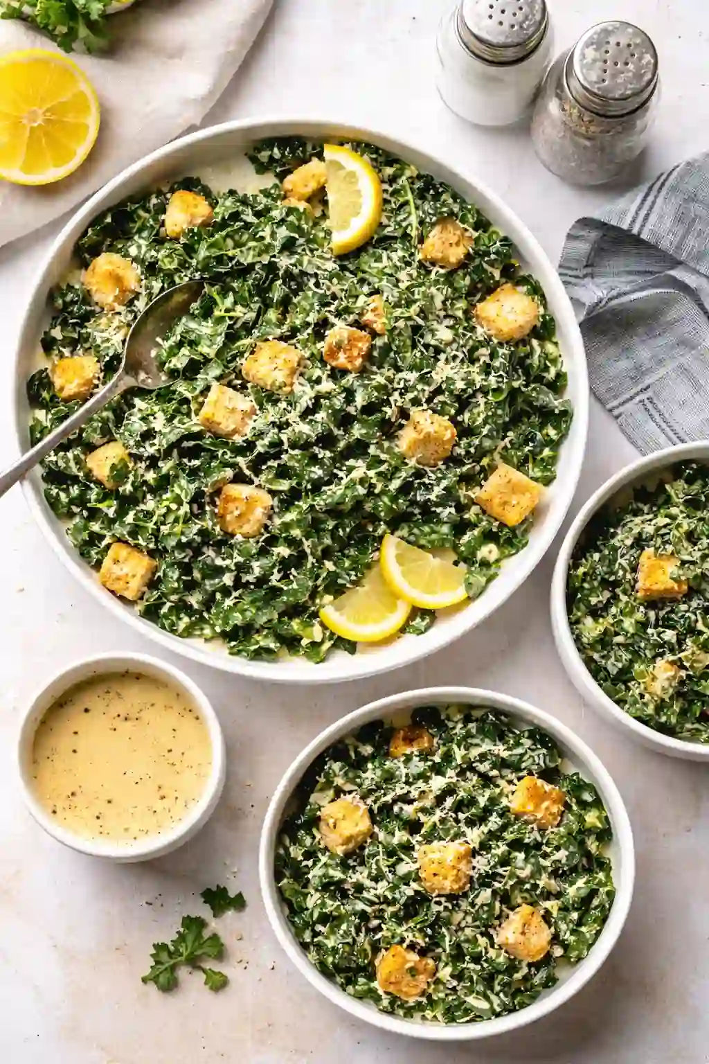 Overhead view of kale caesar salad with chicken served family-style with extra bowls and creamy dressing