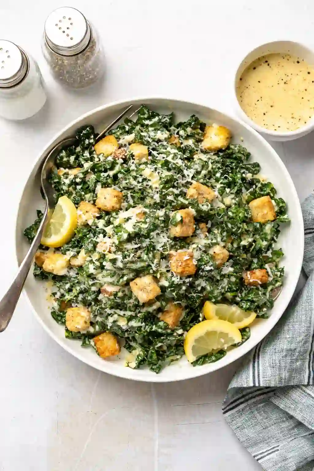 Kale caesar salad with chicken, croutons, and creamy dressing in a white bowl with one spoon
