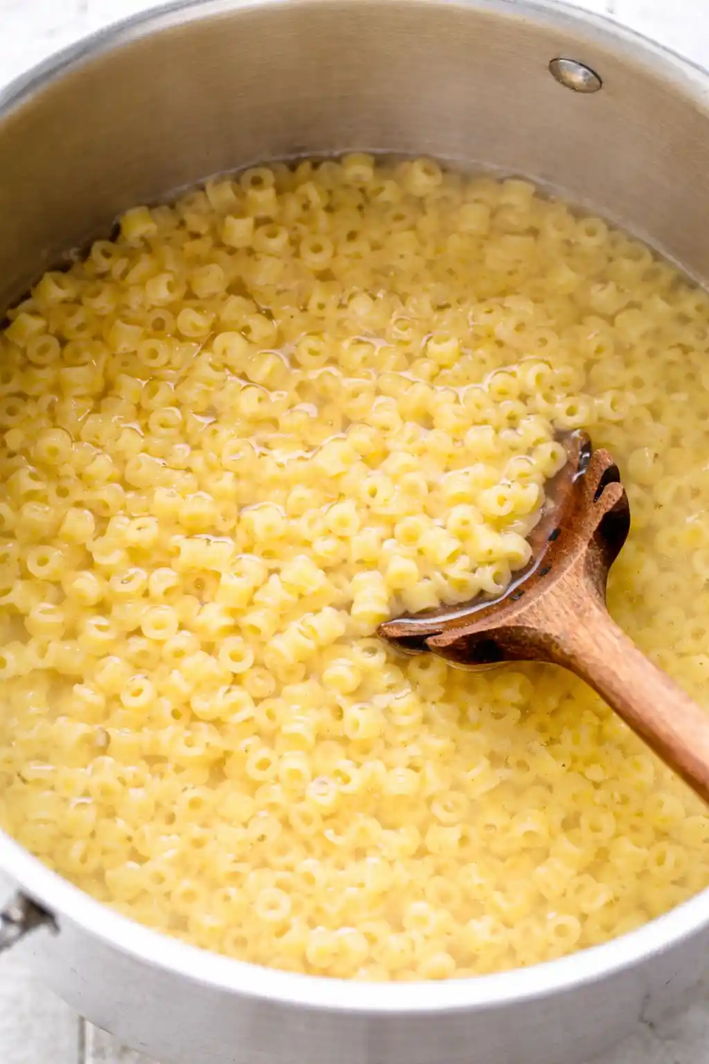 mexican-street-corn-pasta-salad-step-1-cooking-pasta._compressed Ditalini pasta cooking in a stainless steel pot with a wooden spoon on a bright white kitchen surface