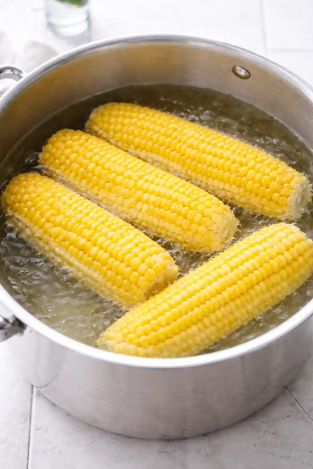 mexican-street-corn-pasta-salad-step-2-boiling-corn._compressed (1) Fresh corn on the cob boiling in a stainless steel pot with bright lighting and no steam