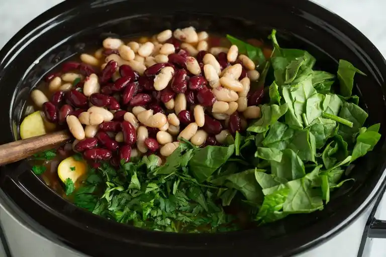 Kidney beans, white beans, spinach, and parsley added to minestrone soup in a slow cooker.