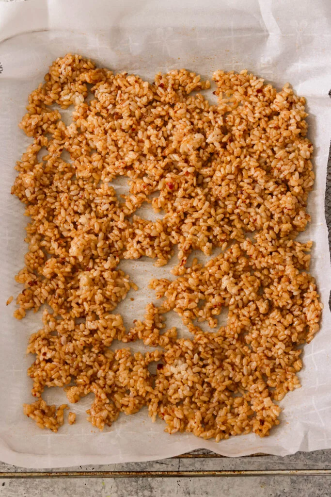 Seasoned rice spread on parchment-lined baking sheet ready for baking