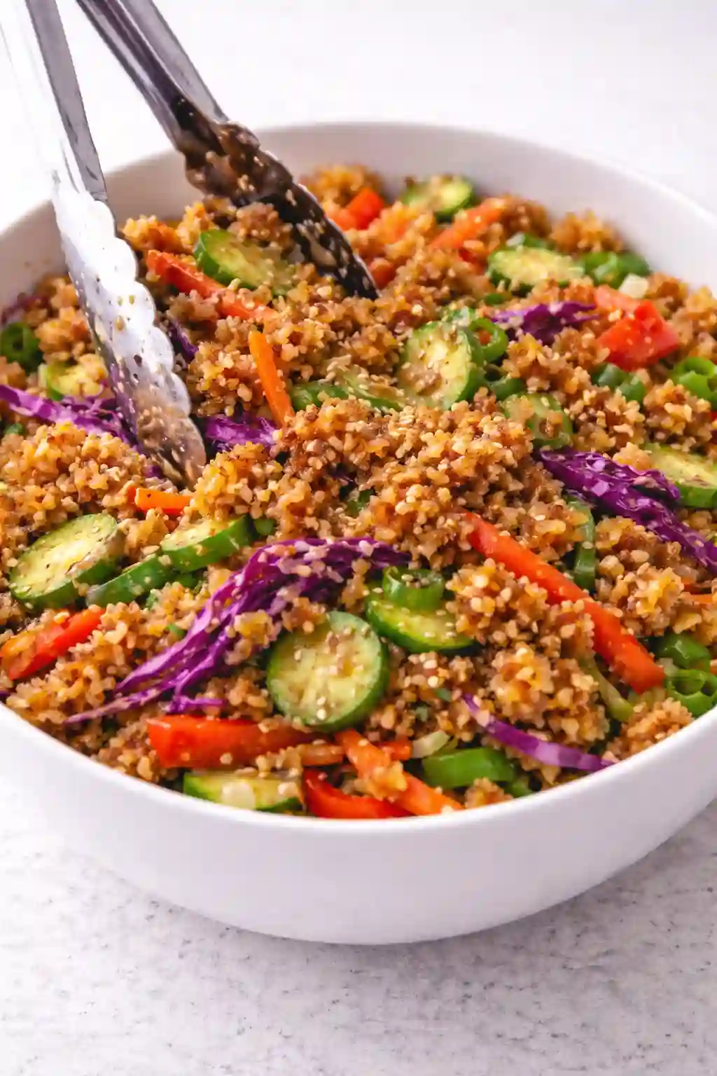 Tossing crispy rice salad with peanut dressing and sprinkling toasted sesame seeds in a white bowl
