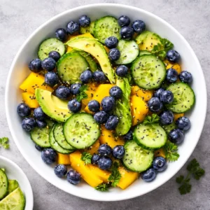 Mango cucumber salad with blueberries and avocado served in a white bowl with fresh ingredients and light dressing