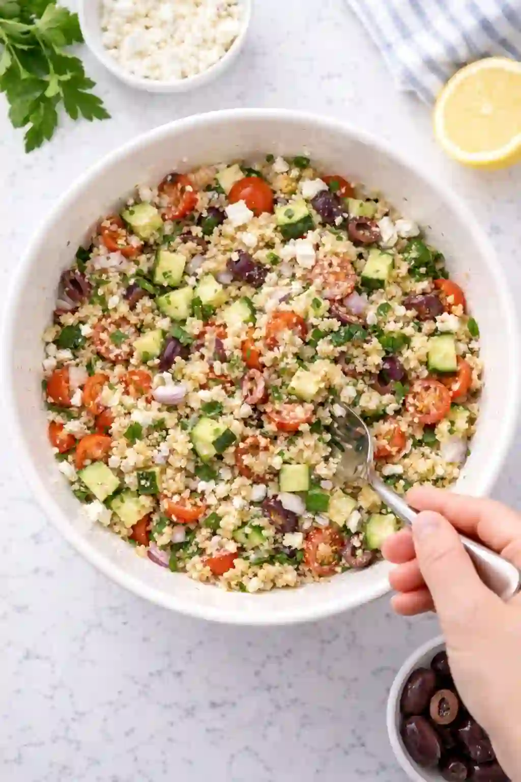 Mixing Mediterranean quinoa salad with cucumber olives peppers and feta
