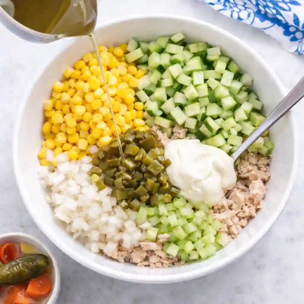 Adding mayonnaise and jalapeño juice to the tuna and vegetables for mexican tuna salad recipe with mayonnaise.