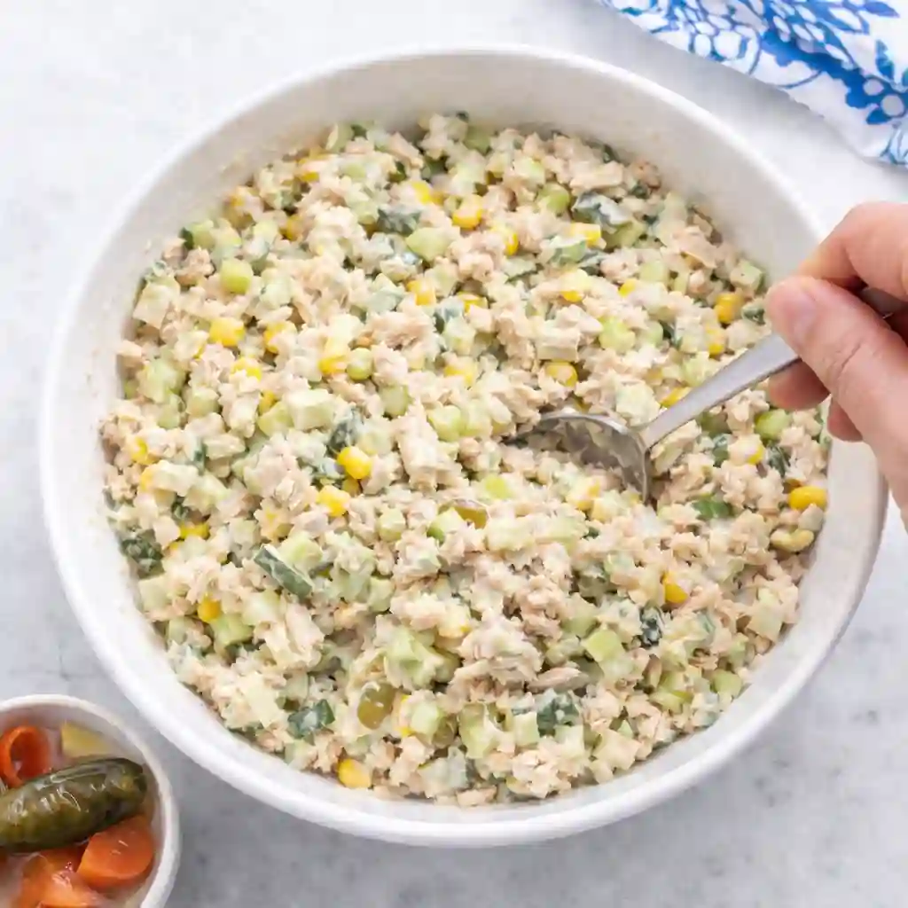 mixing creamy mexican tuna salad with corn cucumber and mayonnaise in white bowl