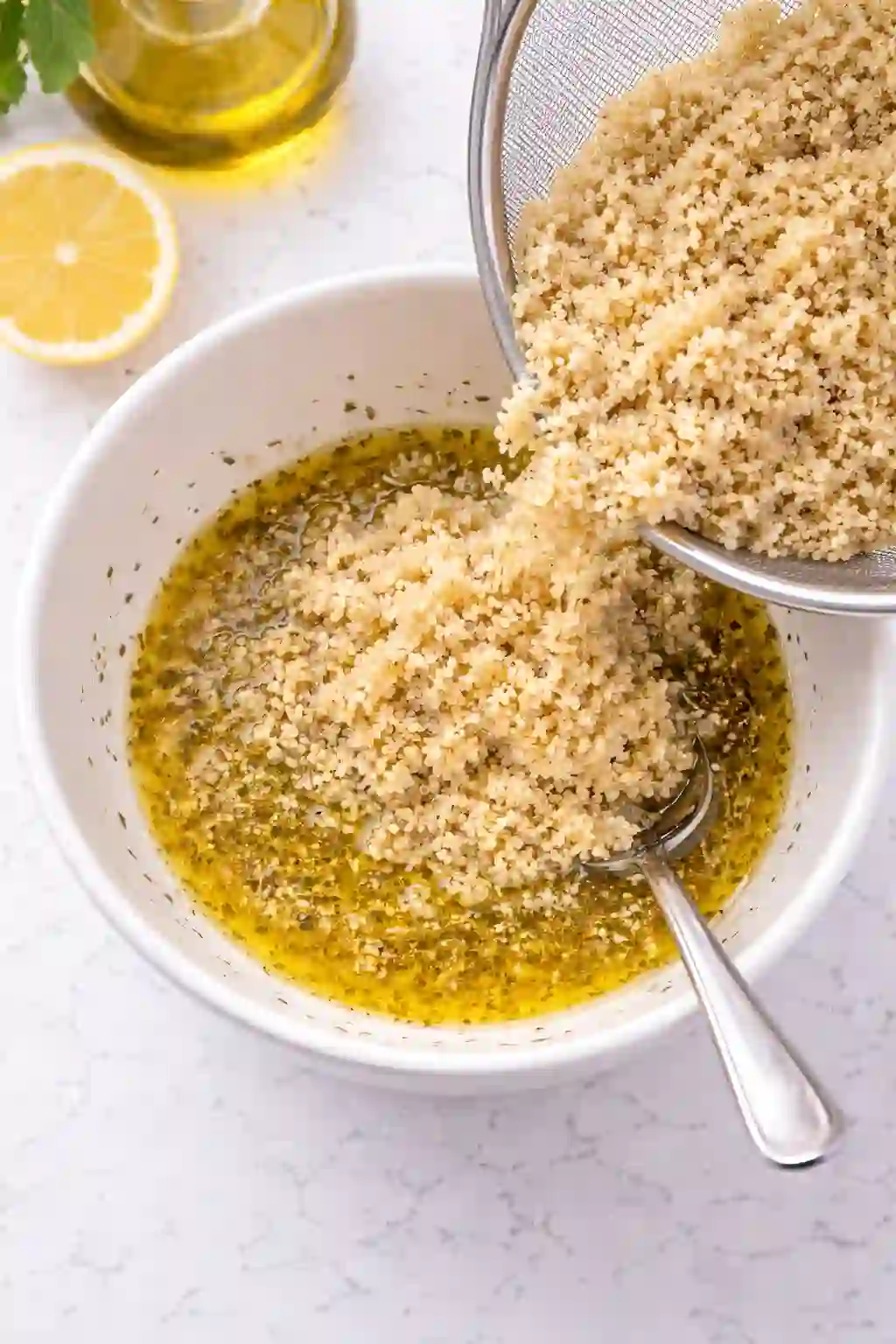 Adding cooked quinoa to lemon olive oil dressing in a bowl