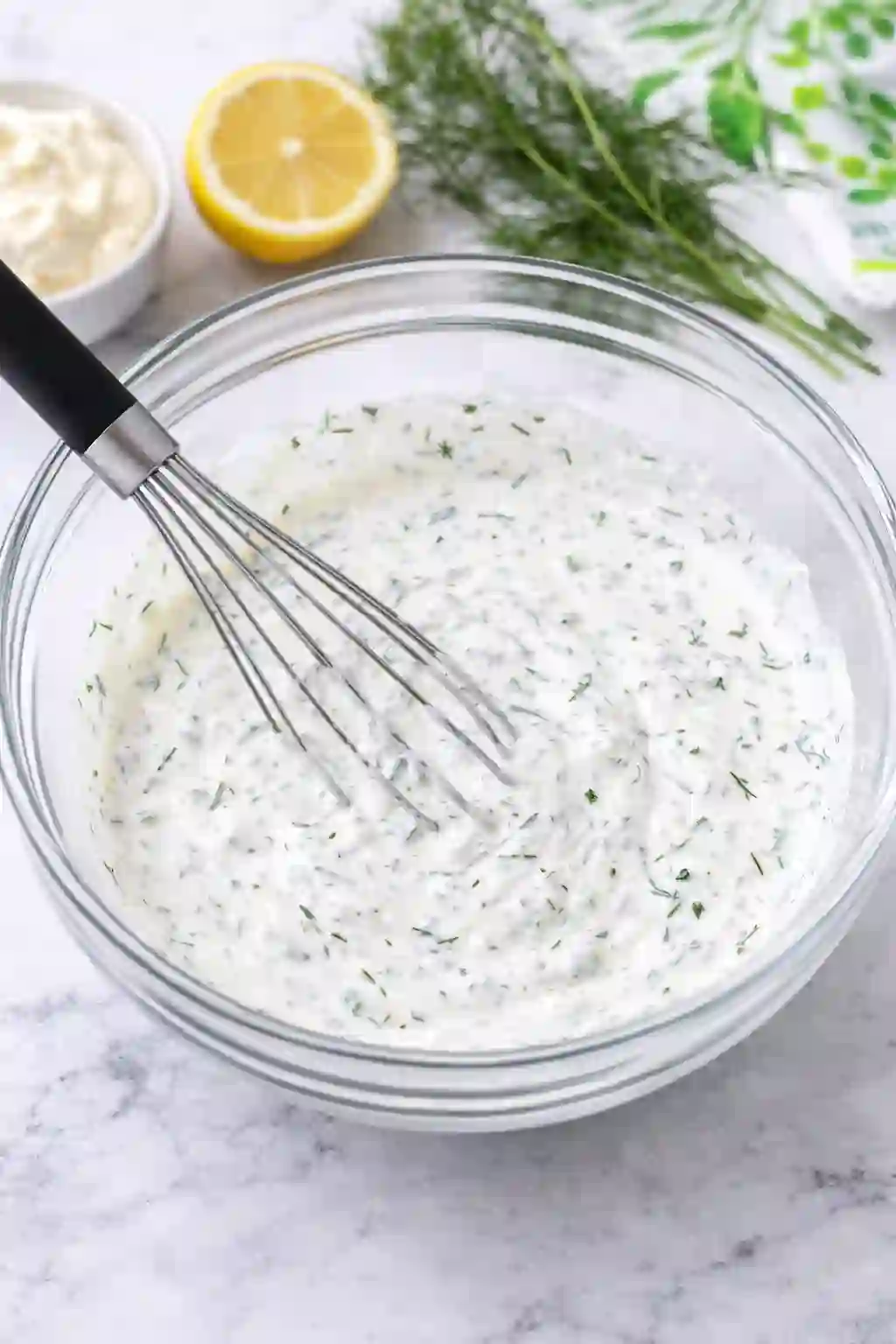 Whisking creamy dressing with dill for creamy cucumber salad in a bowl